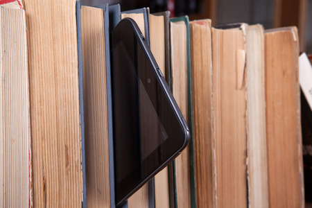 Tablet stands on a bookshelf with old booksの写真素材