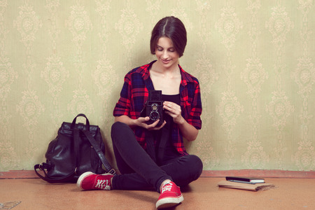 Old vintage film camera in the hands of a young girl in a red plaid shirt sitting near the old yellow wall.の写真素材