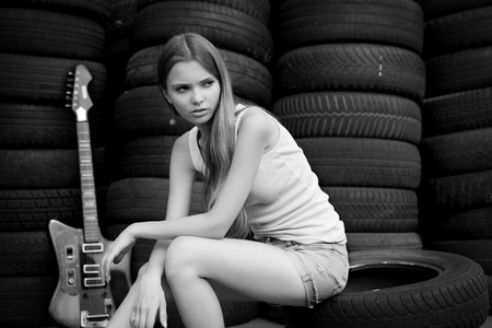 Young girl musician with electric guitar sitting on car tires. Black and white photo.の写真素材