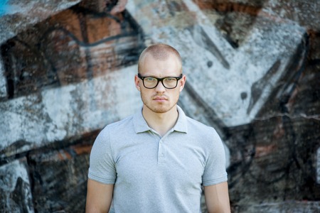 Portrait of a young man against the background of a concrete wall with graffiti. Man in a blue shirt...