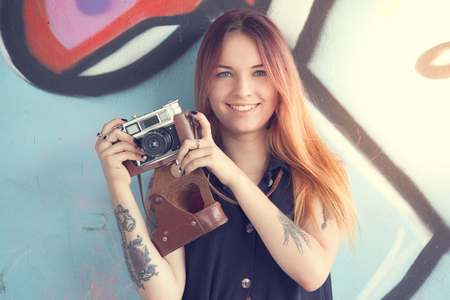 Girl teen with vintage camera against the wall of graffiti looks away. Solar flare in the frame.の写真素材