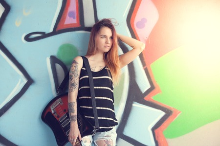 Girl teen with electric guitar stands near the wall of graffiti.の写真素材
