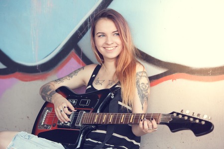 Girl teen sitting near a graffiti wall and plays electric guitar.の写真素材