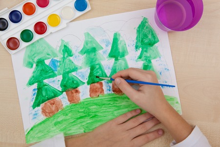 A child paints with watercolors on paper green coniferous forest.の写真素材