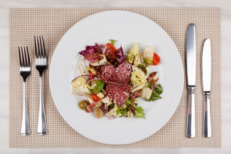 Vegetable salad with sausage on a white plate and cutlery.の写真素材