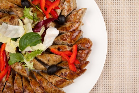 Baked sausage sliced with vegetables on a large platter.