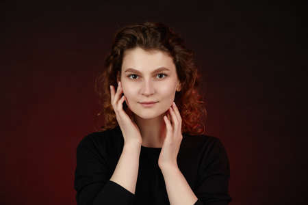 Portrait of a young attractive girl in black clothes on a dark background. Close-up with hands in...