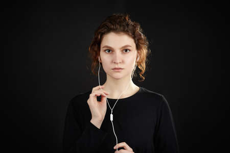 Girl with headphones listens to music. Close-up portrait against a black background.