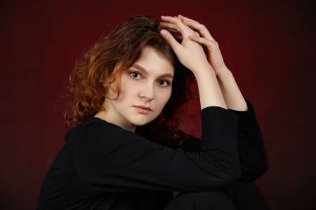 Portrait of a young attractive girl in black clothes on a dark background. Close-up with hands in...