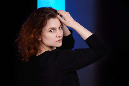 Portrait of a young attractive girl in black clothes on a dark background. Close-up with hands in...
