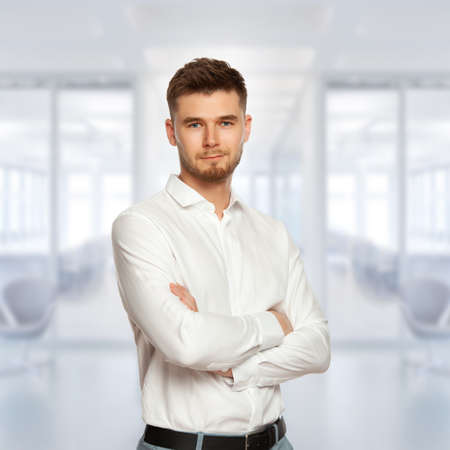 Portrait of a young man. A male office worker stands with his hands folded and looks into the frame.