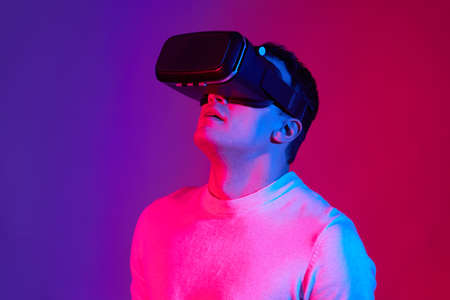 A young man with a virtual reality helmet on his head on a red and blue background.の写真素材
