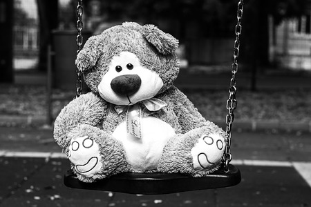 Depressed Fluffy Soft Teddy Bear Toy sitting on cradle in the parkの写真素材