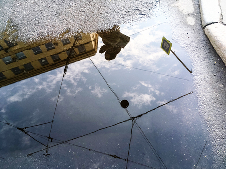 Reflection of a cloudy sky, a public building, tramway wires and a young woman with a phone in hand...