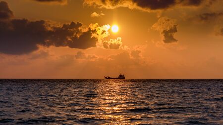 Ship in the horizon at dawn with the sun between clouds in the Maldivian seaの写真素材