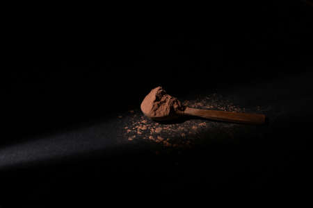Powdered chocolate in a wooden spoon, lit with a soft spot light, on a black background.の写真素材
