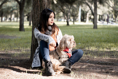 <p>Girl looking into the distance together with her dog in the park. Girl sitting at the foot of a tree together with her dog in the park.</p>の写真素材
