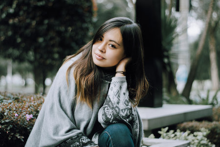 <p>Thoughtful girl sitting alone in a city park. A smiling girl looks at the camera. Medium shot. Sitting girl. Garden in the background</p>の写真素材