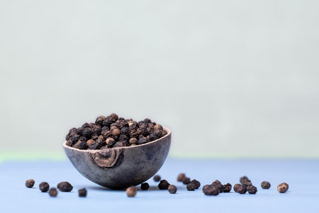 A wooden bowl filled with black pepper. Gray background. A wooden bowl filled with black pepper in a minimalist style. Front view. Scattered black pepperの写真素材