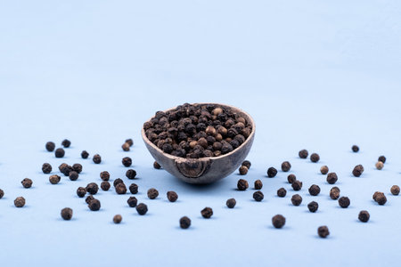 A wooden bowl filled with black pepper in a minimalist style. Front view. Scattered black pepperの写真素材