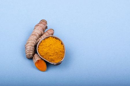 Ground natural turmeric in a wooden bowl accompanied with turmeric root in a minimalist style. overhead view. blue backgroundの写真素材