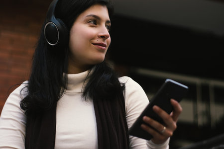 Relaxed girl listening to music while looking into the distance. Woman with her phone listening to music in the cityの写真素材