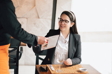 Executive woman receiving the menu in a restaurant. The waiter is handing the restaurant menu to a...