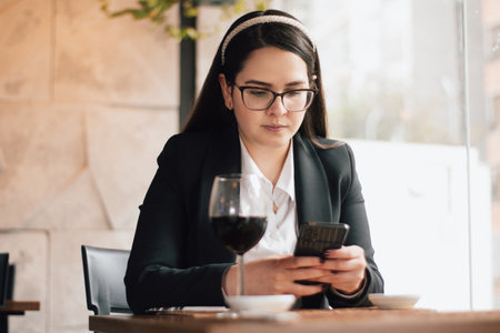 Executive woman looking at her cell phone while waiting for her order in a restaurant. Latin woman chatting with her cell phone in a restaurantの写真素材