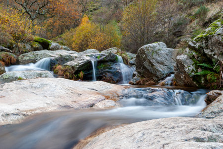 small waterfall in mountain river with long exposure silk effect, with rocks eroded with moss and...