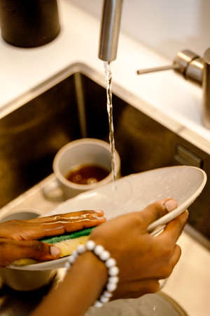 Woman's hands washing dish with scourer and tap waterの写真素材
