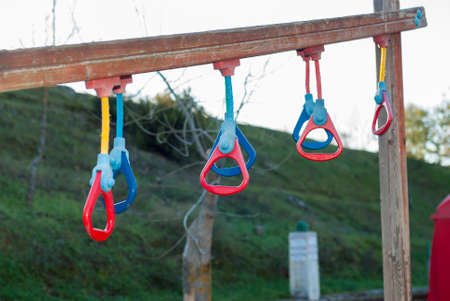 Multicolored gymnastic rings in a playground for outdoor sports, on a wooden bar horizontally