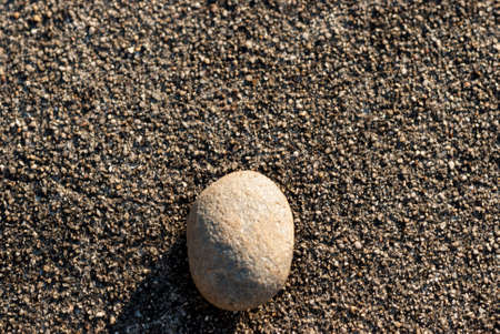 Small white stone isolated on dark gravel background in horizontal with sunの写真素材