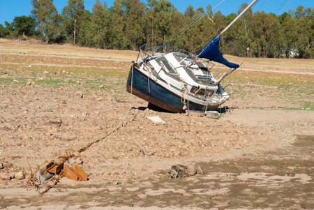 sailboat stranded on land due to drought with blue sky trees in the background horizontalの写真素材