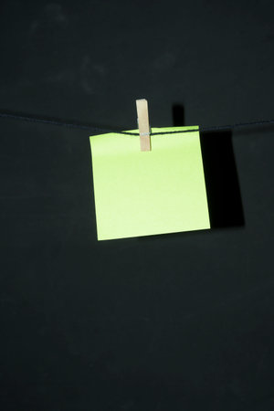 Yellow post it note with wooden clothespin hanging on rope thread with dark background copy space vertical annotationの写真素材
