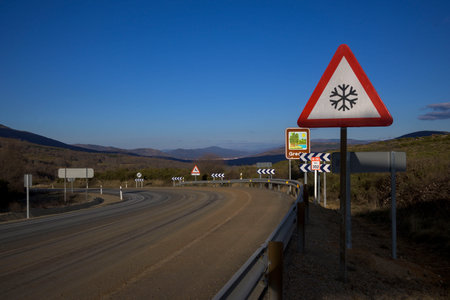 Dangerous curve with tire tracks with warning sign for snow in sunny winter day