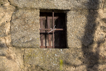 Small wooden window with rusty wrought iron fence in stone wallの写真素材