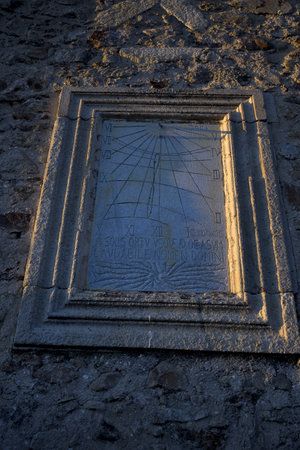 Stone sundial and roman numerals on old stone wall facade vertically