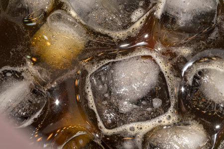 Ice in cold black coffee with foam and bubbles macro photography