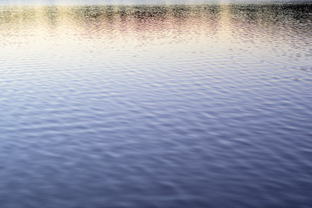 Close up abstract vertical shot of a water surface showing subtle ripples and waves. The color shifts from a warm yellow reflection at the top to a deep blue at the bottom, creating a smooth textureの写真素材