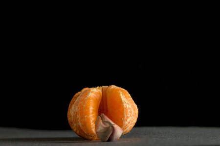 Conceptual still life featuring a partially peeled mandarin orange with a single garlic clove...