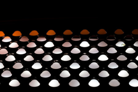 Abstract close up of light shining through the holes of a metal kitchen grater. The backlit pattern creates glowing white and orange semi circles against a dark silhouetted background.の写真素材