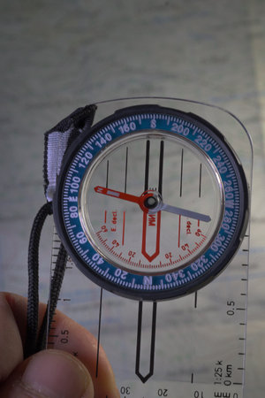 Close up shot of a person's hand holding a compass over a partially obscured topographic map. The fingers and compass are in sharp focus, symbolizing planning and navigation during outdoor adventure.の写真素材