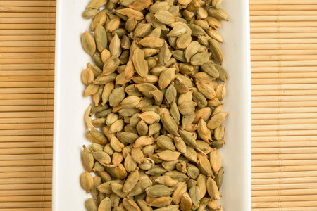 Dried green cardamom pods arranged in a white tray on bamboo mat showing natural texture and warm tones for culinary and spice themesの写真素材