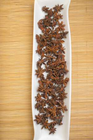 Dried star anise displayed on a white tray over a bamboo mat creating a natural aromatic and culinary spice scene ideal for food conceptsの写真素材