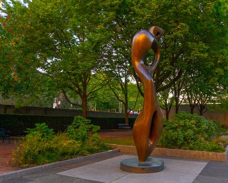 Statue in the middle of a garden, with a beautiful golden orange color. Their ways try to simulate a person. Vivid colors in plants and trees thanks to being an autumn season.の写真素材