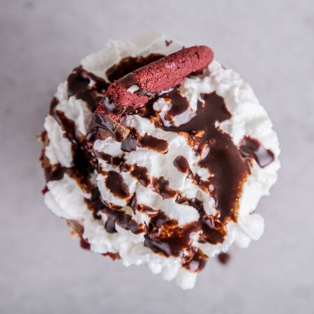 milkshake with whipped cream, pink cookie and chocolate sauce on a grey surface