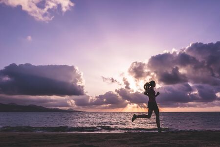 Young woman running on las canteras beach at sunset. Las Palmas de Gran Canaria, Spain. Runing and health care concept.の写真素材