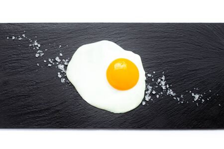 Fried egg on slate plate with salt on white background. Cooking and food concept.の写真素材