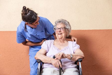 Happy Senior woman with walking stick in Wheelchair with her caregiver at home. They are talking and laughing together.の写真素材