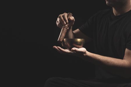 Detail of man sitting playing the Tibetan Singing Bowll in black clothes on black background.の写真素材